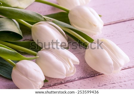 Bouquet of white tulips laying on antique pink wooden table