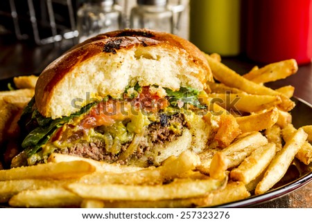 Close up of gourmet pub hamburger with guacamole and caramelized onions on black plate with side of french fries sitting on dark wooden table