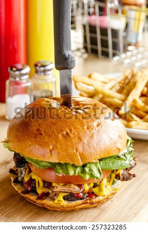 Close up of gourmet pub hamburger with bacon on wooden cutting board with plate of french fries sitting on wooden table