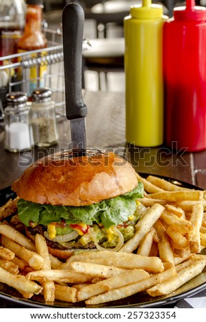 Gourmet pub hamburger with guacamole and caramelized onions on black plate with side of french fries sitting on dark wooden table