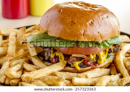 Close up of gourmet pub hamburger with bacon on black plate with french fries sitting on wooden table