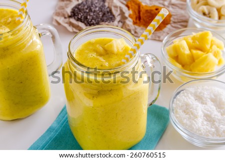 Close up of fresh blended fruit smoothies made with pineapple, banana, coconut, turmeric and chia seeds surrounded by raw ingredients yellow straws