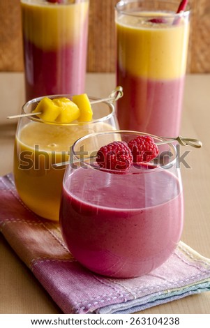 Fresh blended fruit smoothies made with mango, orange, cantaloupe, raspberries, and strawberries garnished with fruit pieces sitting on napkin