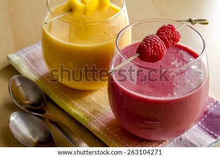 Close up of 2 fresh blended fruit smoothies made with mango, orange, cantaloupe, raspberries, and strawberries garnished with fruit pieces