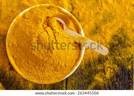 Organic turmeric (curcuma) powder in white bowl with measuring spoon on wooden table