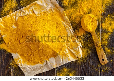 Pile of organic turmeric (curcuma) powder sitting on brown paper with measuring spoon on wooden table