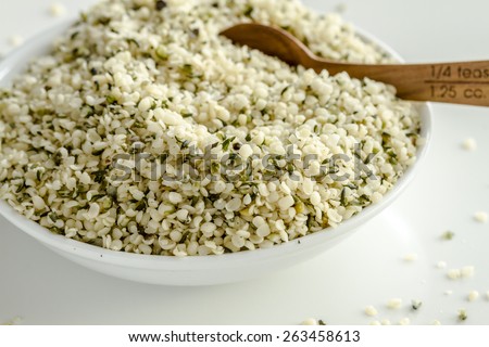 Organic hemp seeds in white bowl with measuring spoon on white background