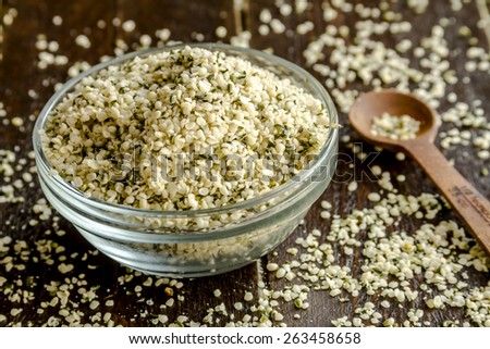 Organic hemp seeds in glass bowl on wooden table with measuring spoon