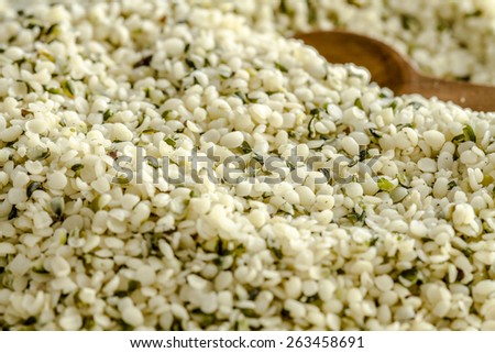 Close up of pile of organic hemp seeds with wooden measuring spoon on white background
