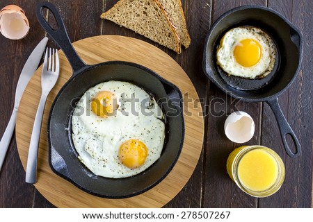 Fried eggs in cast iron skillet sitting on kitchen table with whole wheat toast and orange juice