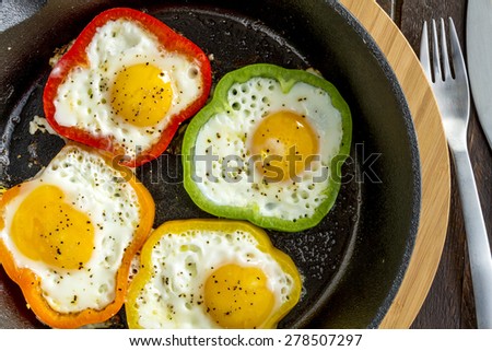 Fried eggs in green, yellow, red and orange bell peppers in cast iron skillet sitting on cutting board
