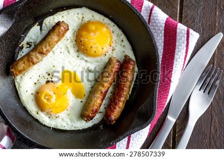Close up of fried eggs and sausage links in cast iron skillet sitting on kitchen table with red striped napkin