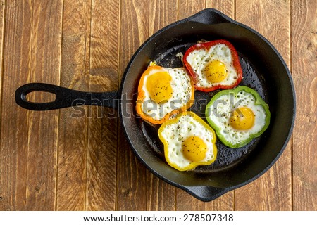 Large cast iron skillet with fried eggs in green, yellow, red and orange bell peppers sitting on wooden table