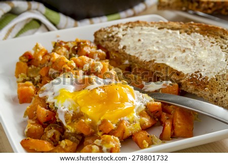 Close up of white plate with single fried egg and sweet potato hash with fork and whole grain toast