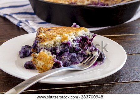 Close up of slice of fresh baked blueberry cobbler sitting on white plate with fork