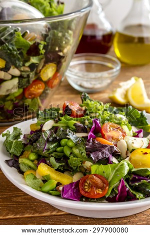 Fresh organic super food salad in white bowl with large bowl, olive oil, red wine  vinegar and lemons in background