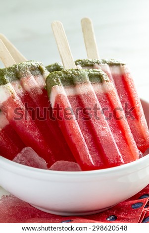 Close up of frozen fresh fruit watermelon and kiwi popsicles in white bowl with ice cubes sitting on watermelon napkins