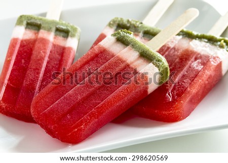 Close up of frozen fresh fruit watermelon and kiwi popsicles sitting on square white plate