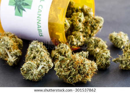 Close up of medical marijuana buds spilling out of prescription bottle with label on black background