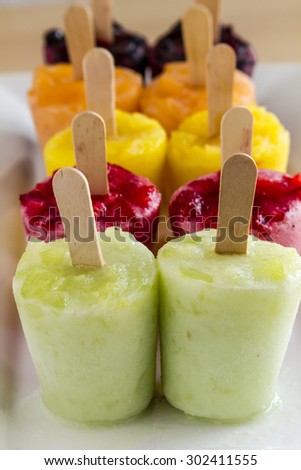 Assorted flavors of homemade fresh pureed frozen fruit popsicles sitting on white plate in a row