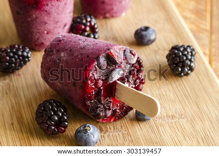 Homemade fresh pureed frozen blueberry and blackberry popsicles sitting on wooden cutting board with fresh berries