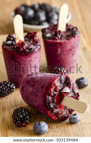 Homemade fresh pureed frozen blueberry and blackberry popsicles sitting on wooden cutting board with fresh berries