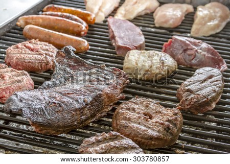 Hamburgers, bratwurst, sausages, tri-tip beef, filet mignon steaks and chicken cooking on grill at summer picnic