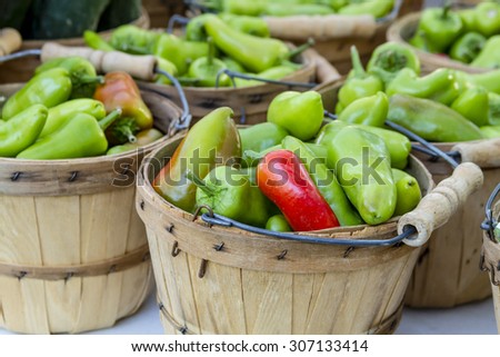 Fresh organic green and red fresno peppers in brown bushel baskets sitting on table at local farmers market