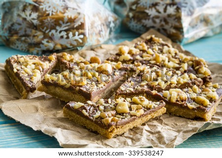 Close up of homemade shortbread cookies coated with chocolate and walnuts sitting on brown paper with food gift packages in background