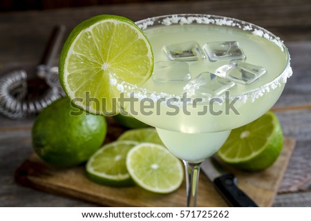 Classic lime margarita cocktail with sliced and whole limes sitting on wooden cutting board