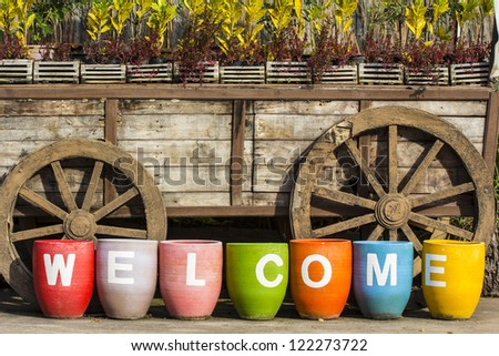 old wooden wheel and colorful Flower pot arranged as WELCOME