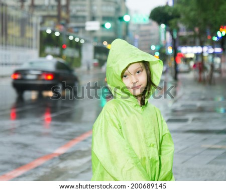 Young girl in rain wearing a green raincoat next to a city street