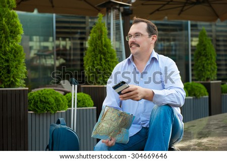 Traveler with mobile phone and city plan sitting outdoors.