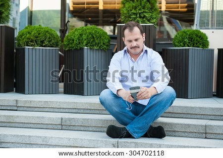 Urban man using smart phone outside using app on 4g wireless device wearing headphones. Sittin in yoga pose