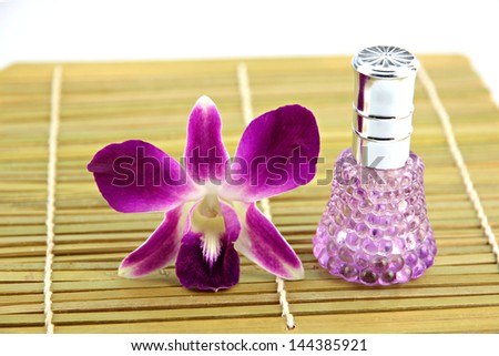 Purple orchid and perfume bottles in bamboo dish on white background.