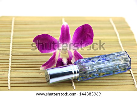 Purple orchid and blue perfume bottles in bamboo dish on white background.