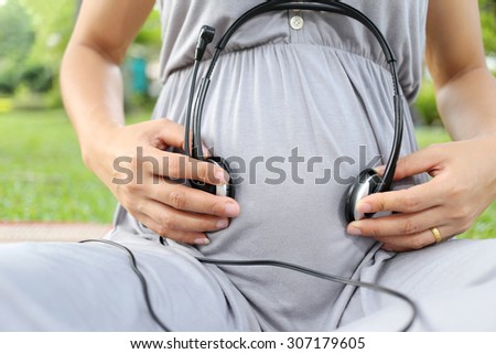 Pregnant women put earphone in hand on her belly for development of hearing to baby.