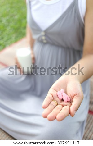 Pregnant women have a glass of Milk and vitamin pill in hand to eat for health of the baby.