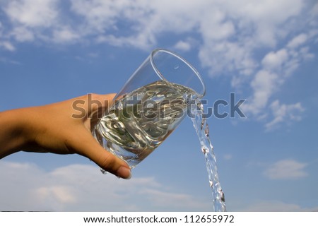 Hand holding glass with water pouring down