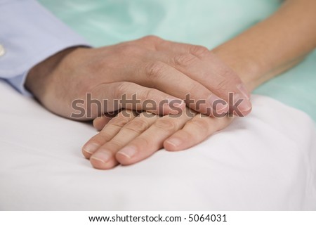 Hands clasping on hospital bed.