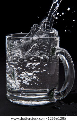 pouring water in glass cup isolated on black background