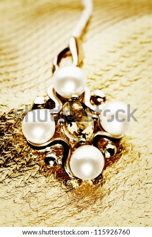 Gold pendant with jewels on the golden background.