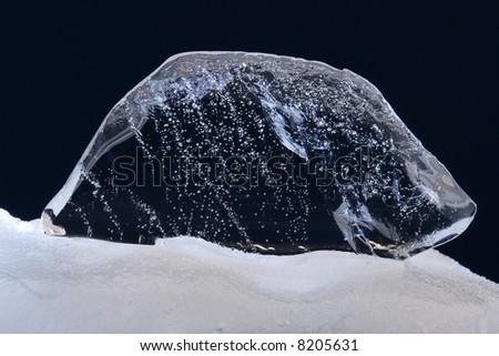 Thawing clear ice fragment on the snowdrift.