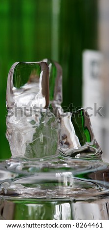 Thawing ice cubes on the glass in front the green bottle.