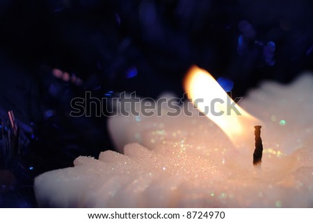 Snowflake-shaped candle on the dark blue background. Narrow depth of field.