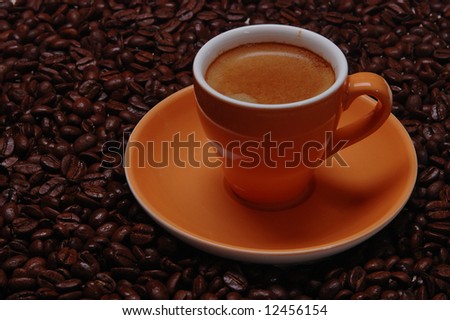 Orange-colored ceramic cup of coffee on the coffee beans.