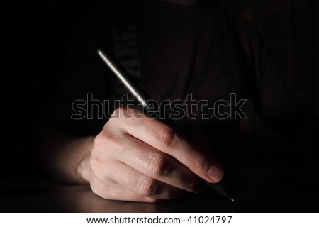 Pen in the male hand. Dark background.