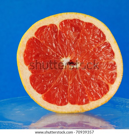 Big piece of red grapefruit on the glass. Blue background.