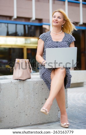 Happy and Smiling old senior business woman 60-65 years, using and typing keyboard on laptop computer in New York city park, looking to front