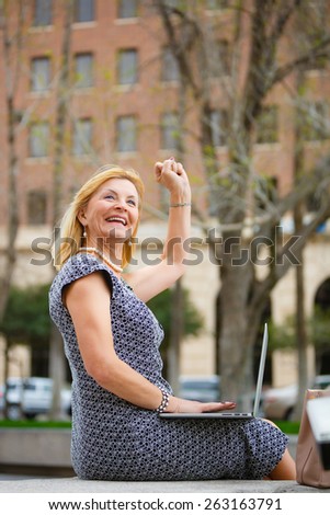Close Up portrait, Happy and Smiling old senior business woman 60-65 years, using laptop computer on your lap in New York city park, looking to up, with gesture on face, emotions raised hand up